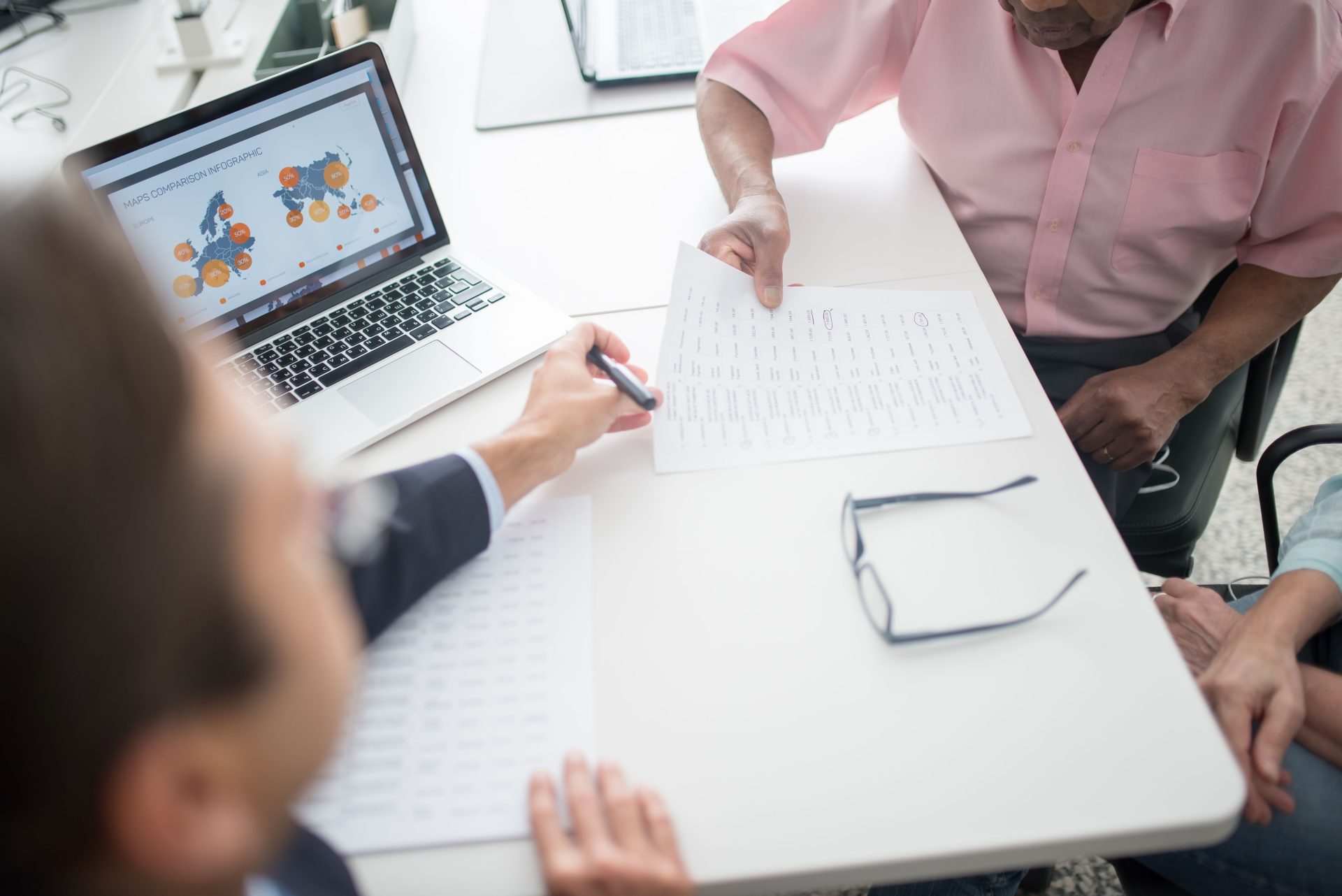 Un couple de personnes âgées examine des documents avec un consultant à un bureau équipé d'un ordinateur portable.